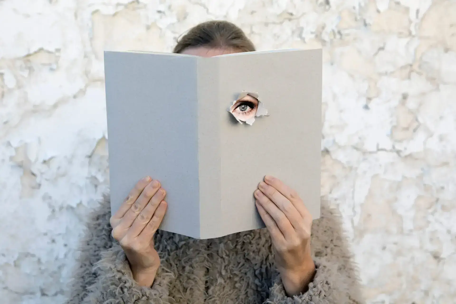 Woman covering face with book, reading poetry, eye looking through cover Woman covering face with book, reading poetry, eye looking through cover